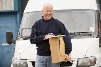 Deliveryperson standing with van with clipboard and box smiling