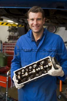 Mechanic holding car part smiling