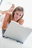 Woman lying in bed with laptop smiling
