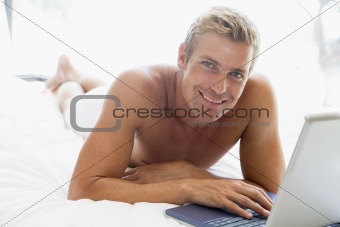 Man lying in bed with laptop smiling