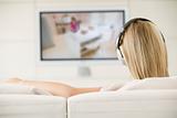 Woman in living room watching television and wearing headphones