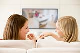 Two women in living room watching television eating chocolates s