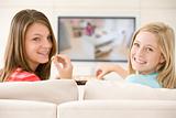 Two women in living room watching television eating chocolates s