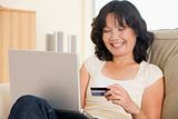 Woman in living room using laptop holding credit card and smilin