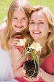 Mother and daughter outdoors holding flower smiling