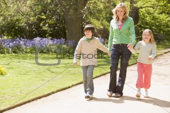 Mother and two young children walking on path holding hands smil