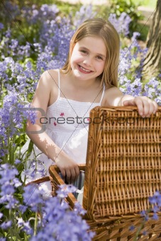 Young girl sitting outdoors with picnic basket smiling