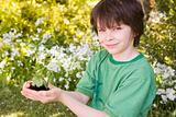 Young boy outdoors holding plant smiling