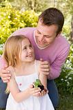 Father and daughter outdoors holding plant smiling