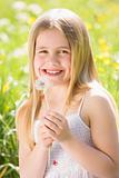 Young girl sitting outdoors holding dandelion head smiling