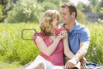 Couple sitting outdoors holding flower smiling