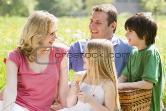 Family sitting outdoors with picnic basket smiling