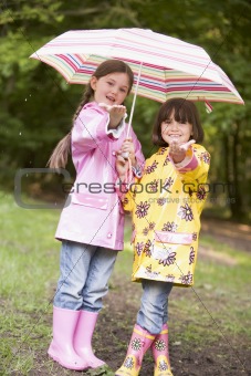 Two sisters outdoors in rain with umbrella smiling