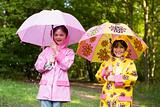 Two sisters outdoors in rain with umbrellas smiling