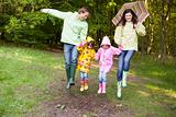 Family outdoors skipping with umbrella smiling