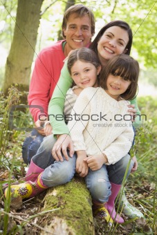 Family outdoors in woods sitting on log smiling