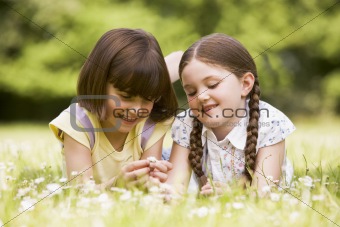 Two sisters lying outdoors with flower smiling