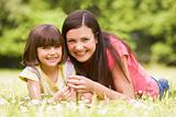 Mother and daughter lying outdoors with flower smiling
