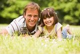 Father and daughter lying outdoors with flowers smiling