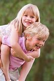 Young boy giving young girl piggyback outdoors smiling