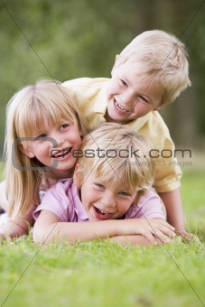 Three young children playing outdoors smiling
