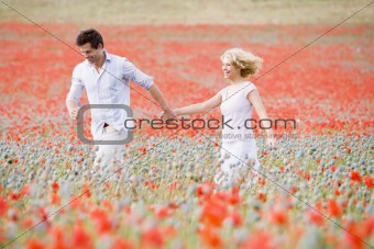 Couple walking in poppy field holding hands smiling