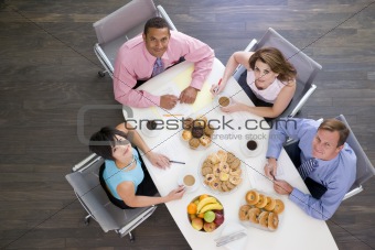 Four businesspeople at boardroom table with breakfast smiling