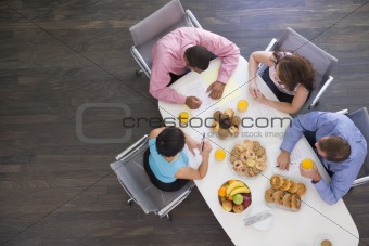 Four businesspeople at boardroom table with breakfast