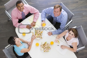 Four businesspeople at boardroom table with sandwiches smiling