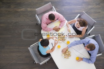 Four businesspeople at boardroom table with sandwiches