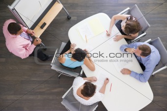Four businesspeople at boardroom table watching presentation