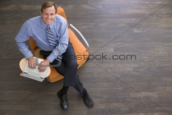 Businessman sitting indoors with laptop smiling