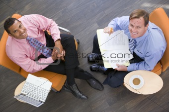 Two businessmen sitting indoors with coffee laptop and folder sm