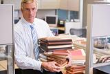 Businessman standing in cubicle holding stacks of files