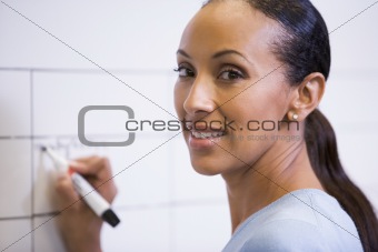 Businesswoman indoors writing on erasable board smiling