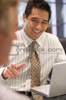 Two businessmen in boardroom with laptop talking
