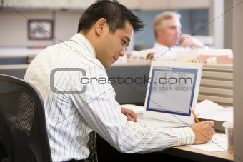 Businessman in cubicle with laptop writing