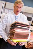 Businessman standing in cubicle with stacks of files
