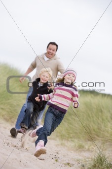 Father and two young children running at beach smiling