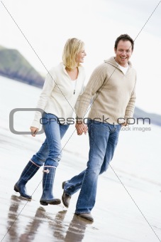 Couple walking on beach holding hands smiling