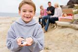Family at beach with picnic smiling focus on boy with seashells