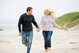 Couple running at beach holding hands smiling