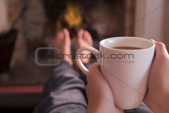 Feet warming at fireplace with hands holding coffee