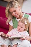 Mother in living room reading book with baby smiling