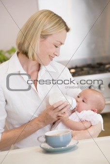 Mother feeding baby in kitchen with coffee smiling