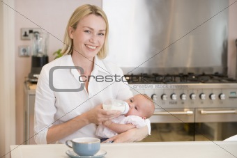 Mother feeding baby in kitchen with coffee smiling
