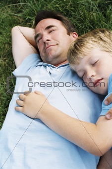 Father and son lying outdoors sleeping