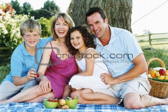 Family sitting outdoors with picnic smiling