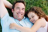 Father and sleeping daughter lying outdoors smiling