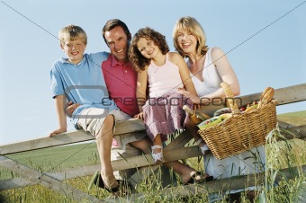 Family outdoors by fence with picnic basket smiling